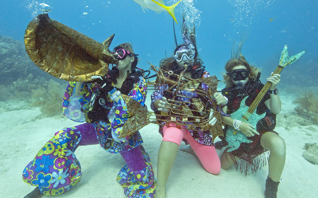 A yellowtail snapper swims by participants pretending to play a local artist's musical instrument sculptures at the Lower Keys Underwater Music Festival Saturday, July 8, 2017, in the Florida Keys National Marine Sanctuary off Big Pine Key, Fla. The event at Looe Key Reef attracted about 400 divers and snorkelers who got wet to listen to a Keys radio station's special four-hour broadcast with music and coral reef conservation announcements piped beneath the sea. From left are Kama Cannon, Marsella Munoz and Madeline Schoepf. FOR EDITORIAL USE ONLY (Bob Care/Florida Keys News Bureau)/HO