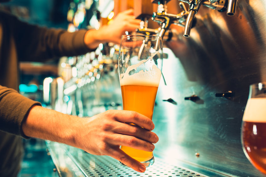 Hand of bartender pouring a large lager beer in tap. Soft, vintage instagram effect on photo. Pouring beer for client. Side view of young bartender pouring beer while standing at the bar counter