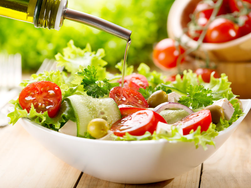 olive oil pouring into bowl of salad